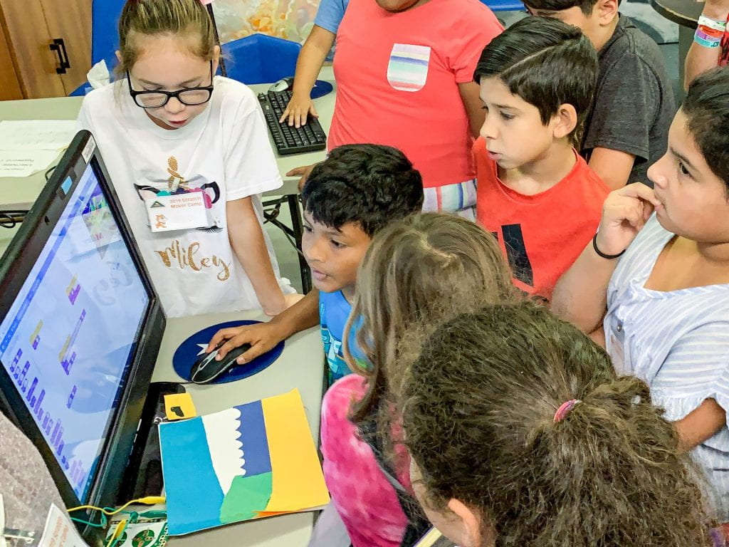 Children gather around a computer to solve a challenge.
